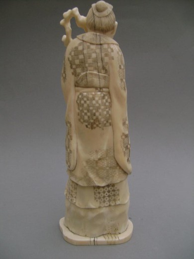 Ivory okimono depicting a tall Sage standing on a rock, with a long gnarled stick and holding a rabbit against him. Some lines of age, weak patina, signature under the base GYOKUSEN, origin Japan around 1910