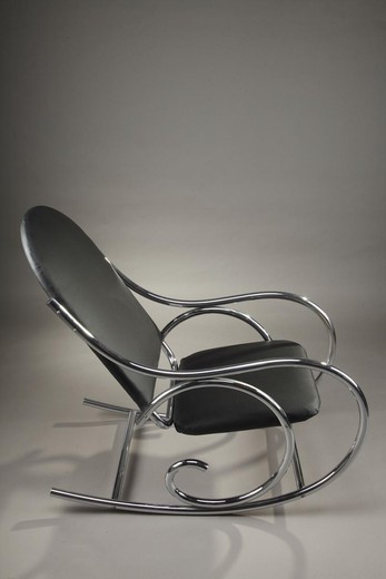 1950s rocking chair in Thonet style. It is composed of a black leatherette upholstered seat and back with oval top, above scrolling arms and undulating legs.
