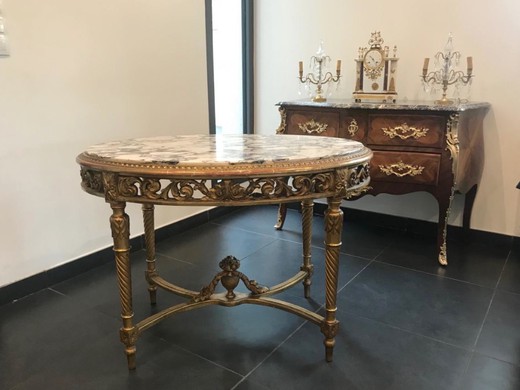 An antique table in the style of Louis XVI. It is made of wood with gilding. The table top is marble. France, 1900s.