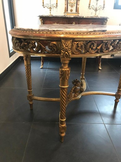An antique table in the style of Louis XVI. It is made of wood with gilding. The table top is marble. France, 1900s.