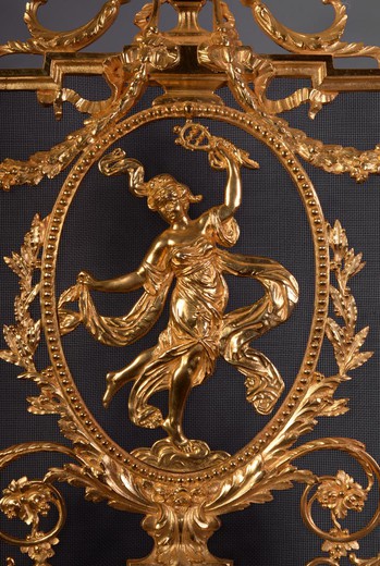 This antique Napoleon III style firescreen was made in the 19th century. In the center, in a richly ornamented medallion, a barefoot dancer wearing an antique dress made of draperies is represented. The firescreen has a very opulent decor typical of the N
